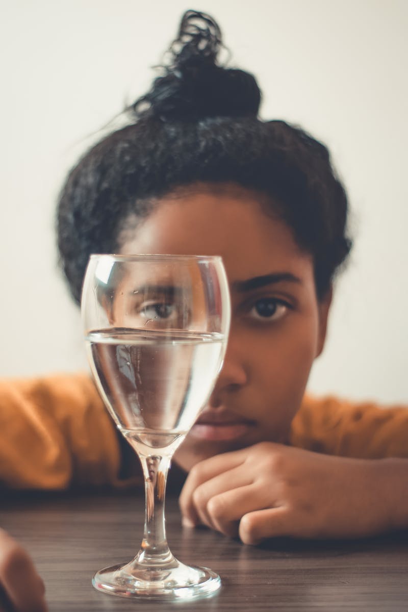 Jovem mulher negra olhando para copo com água à frente - Metrópoles