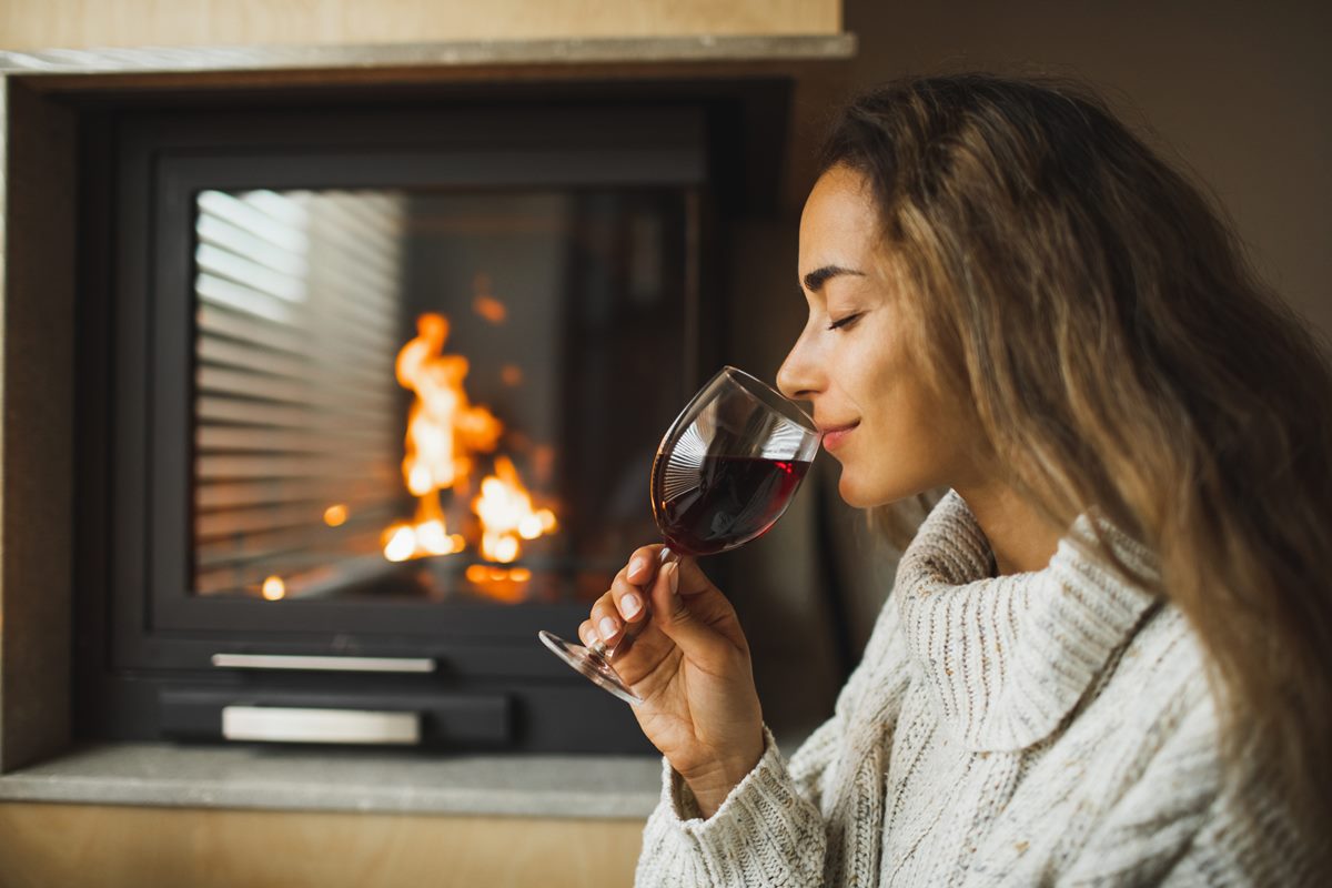 Mulher bebendo vinho perto de uma lareira 