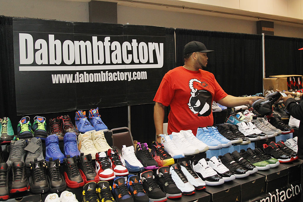 Homem de boné preto e camisa vermelha com seu stand de revendas rodeado de Jordans.