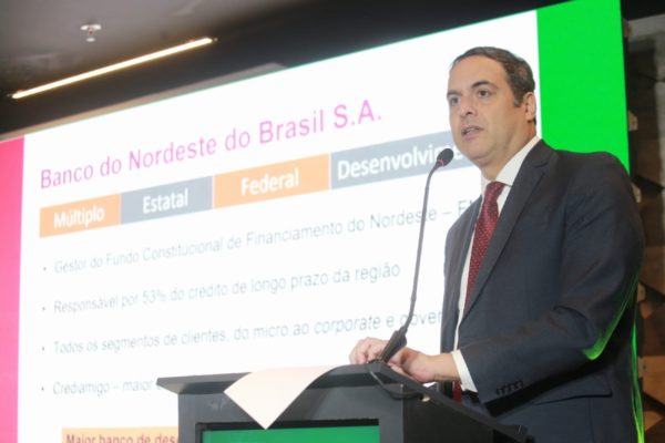 Fotografia colorida mostrando homem discursando em pupito com telão atrás mostrando dados econômicos-Metrópoles