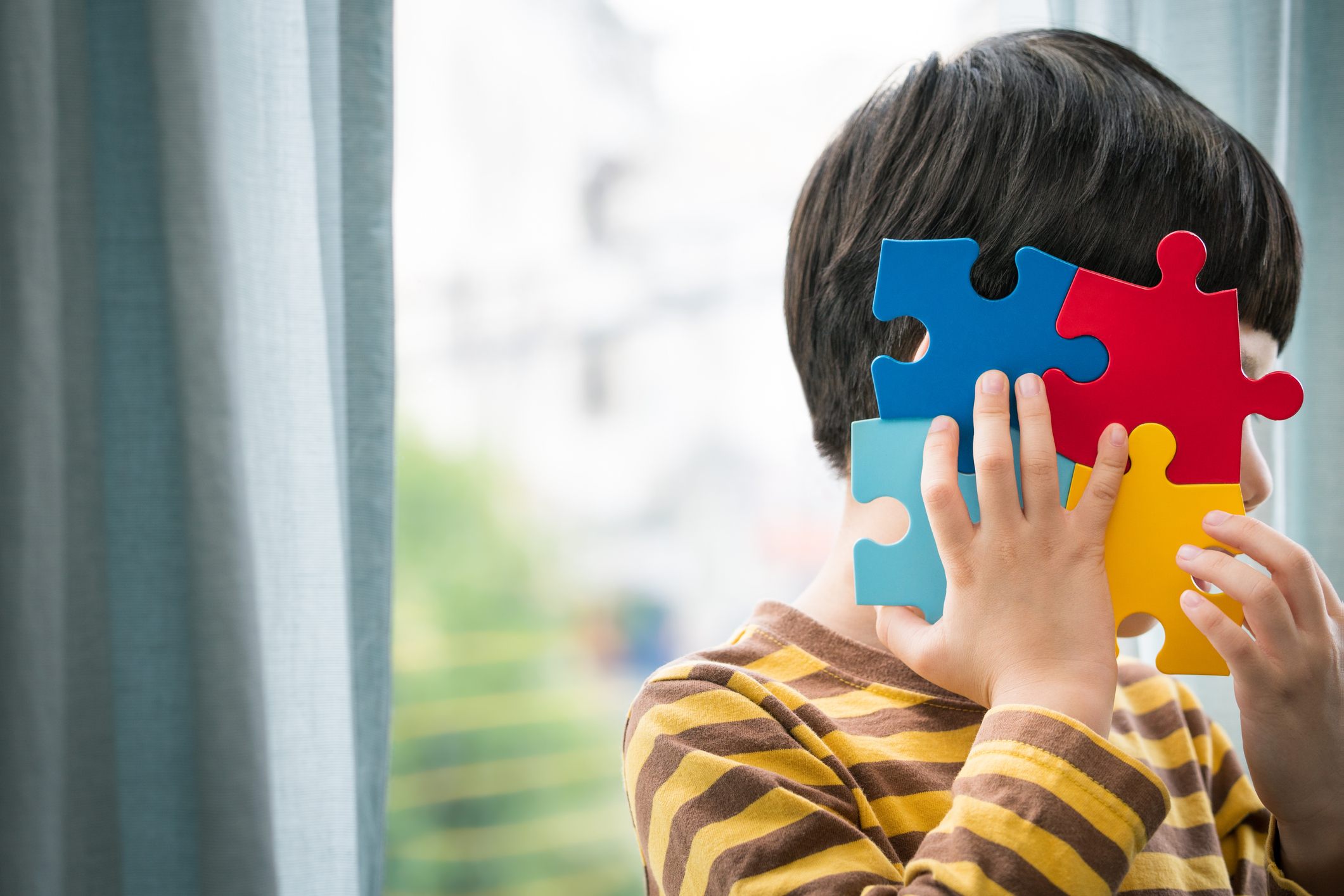 Foto mostra criança cobrindo o próprio rosto com o símbolo do autismo como se fosse uma máscara