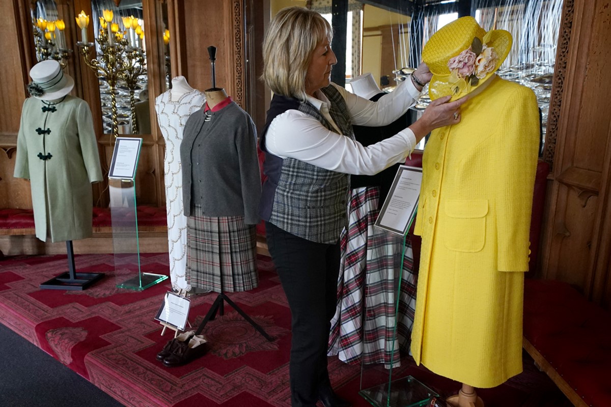 Curadora Sarah Hoare fazendo ajustes nas roupas da rainha Elizabeth II, expostas no castelo Balmoral