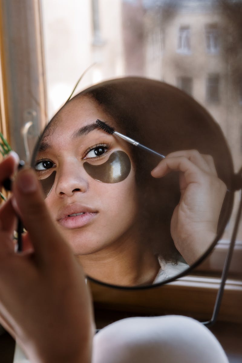 Jovem mulher negra penteando as sobrancelhas de frente para o espelho - Metrópoles