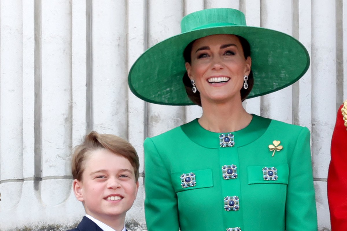 Foto de menino loiro sorridente ao lado de mulher com roupa e chapéu verde - Metrópoles