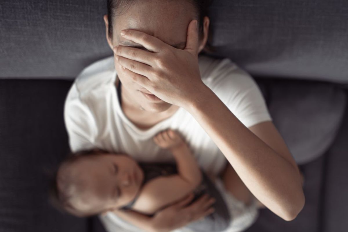 Mulher com a mão no rosto e segurando um bebe no colo