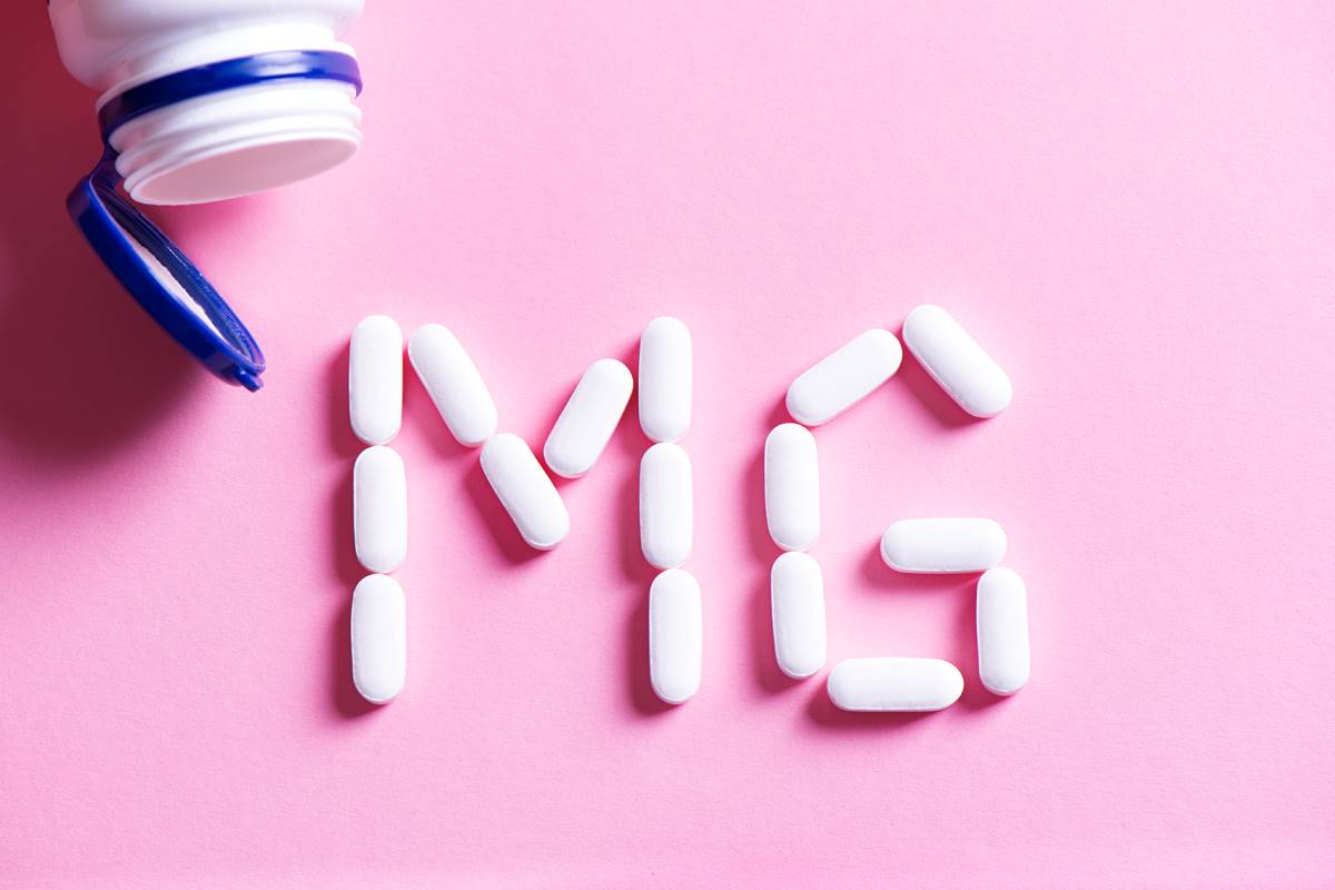 Pote de suplementos aberto em cima da mesa com pílulas formando "MG"