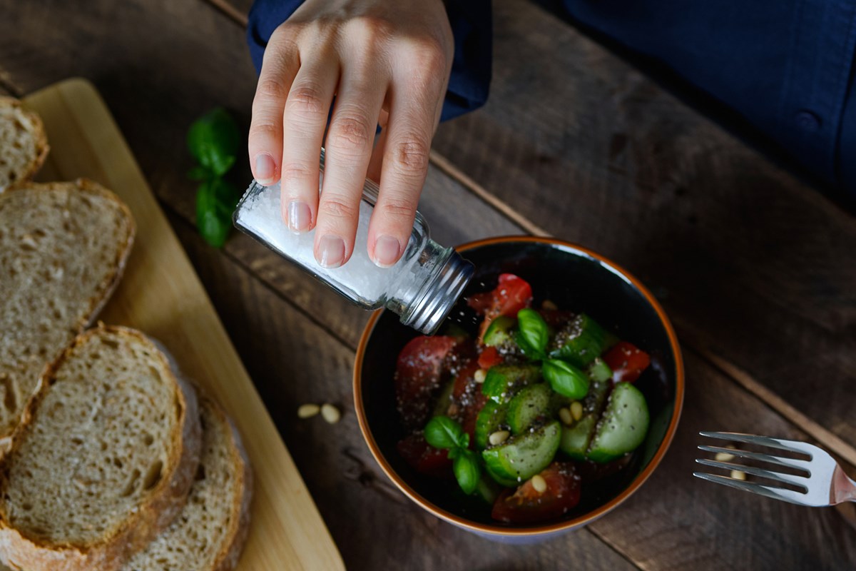 Foto colorida de mão segurando pote de sal sendo colocando em legumes dentro de pote - Metrópoles