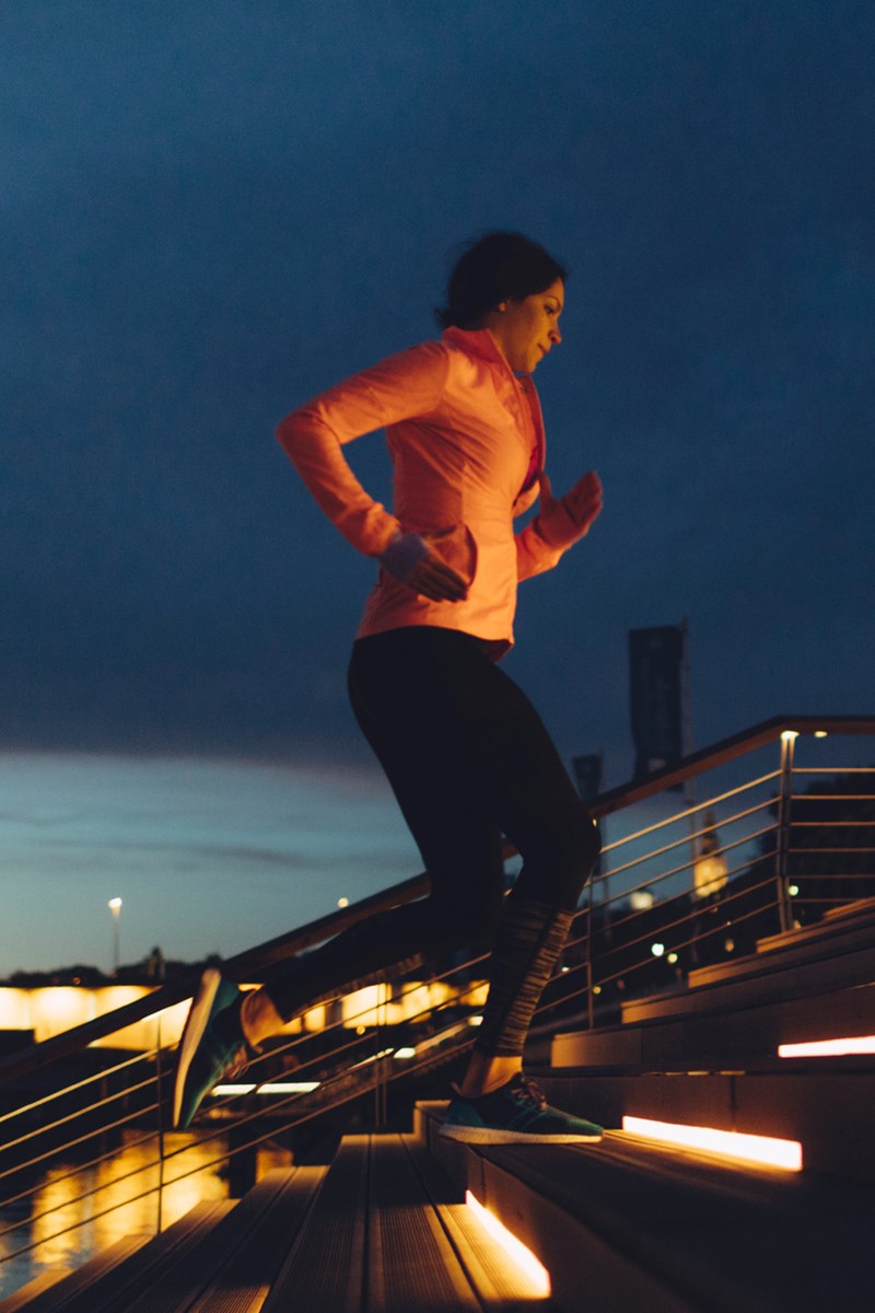 Foto colorida de mulher subindo escada iluminada à noite - Metrópoles