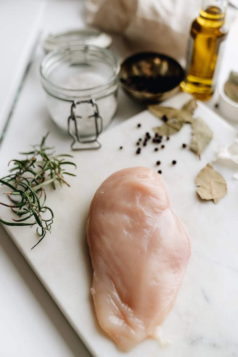 Peito de frango cru sendo preparado para refeição com temperos ao redor - Metrópoles