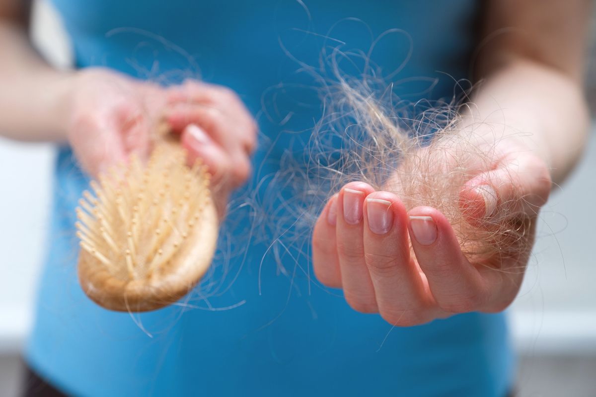 Fotografia colorida mostrando mulher tirando fios de cabelo de escova-Metrópoles