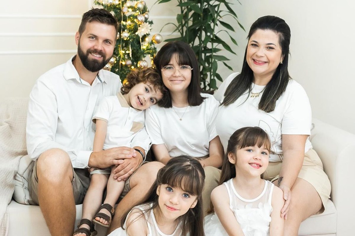 Foto colorida de homem e mulher rodeados por três meninas e um menino. Atrás deles tem um árvore de Natal - Metrópoles