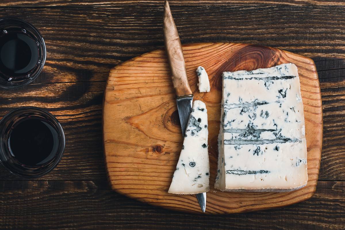 Imagem colorida - tábua com um pedaço de queijo gorgonzola, que tem pontos azuis 