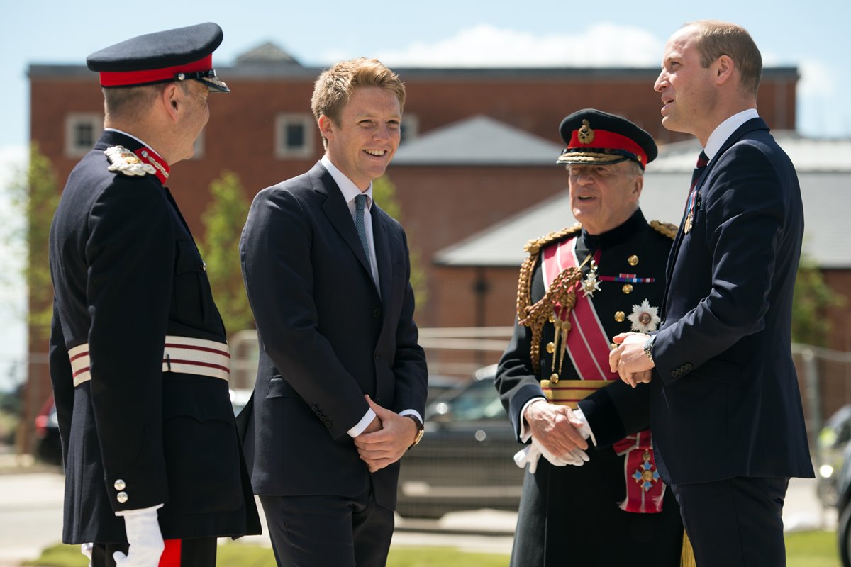 Foto colorida de quanto homens conversando. Dois estão com terno e dois deles vestem trajes militares britânicos - Metrópoles