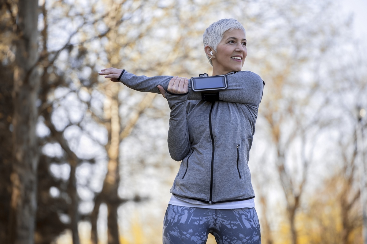 Mulher sênior do atleta que faz o exercício do aquecimento antes do exercício na natureza.