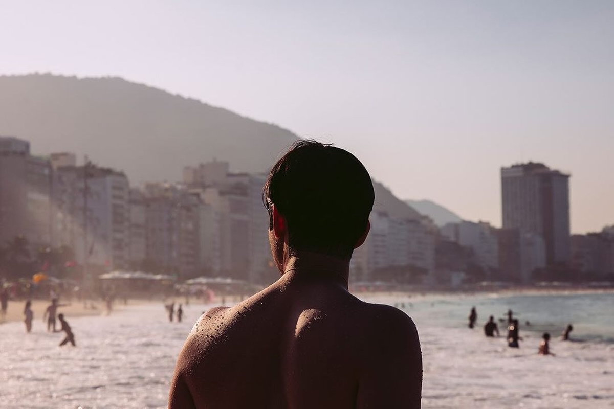 Foto colorida de homem de costas em praia - Metrópoles