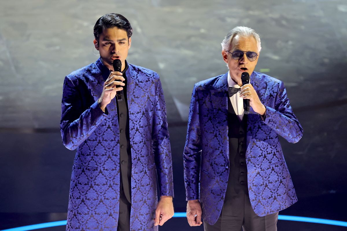 Foto colorida de dois homens cantando. Eles usam uma roupa igual - Metrópoles