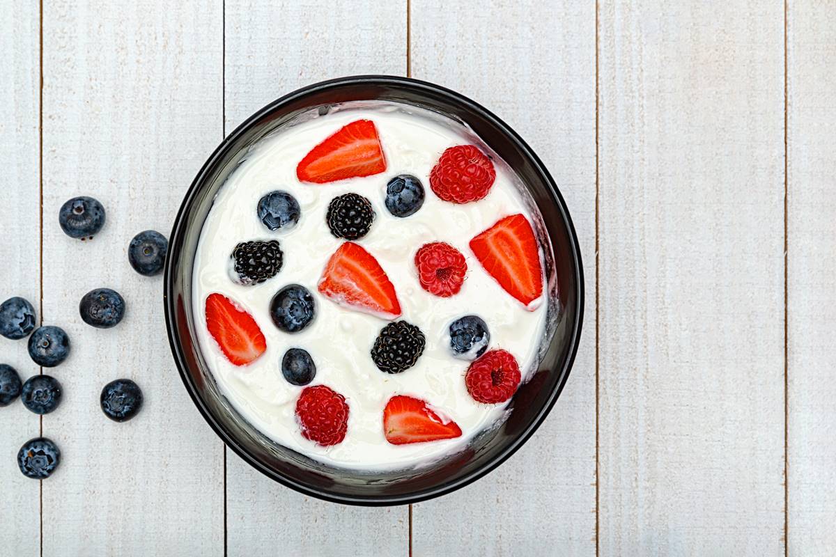 Foto colorida - Pote com iogurte, morangos e mirtilos