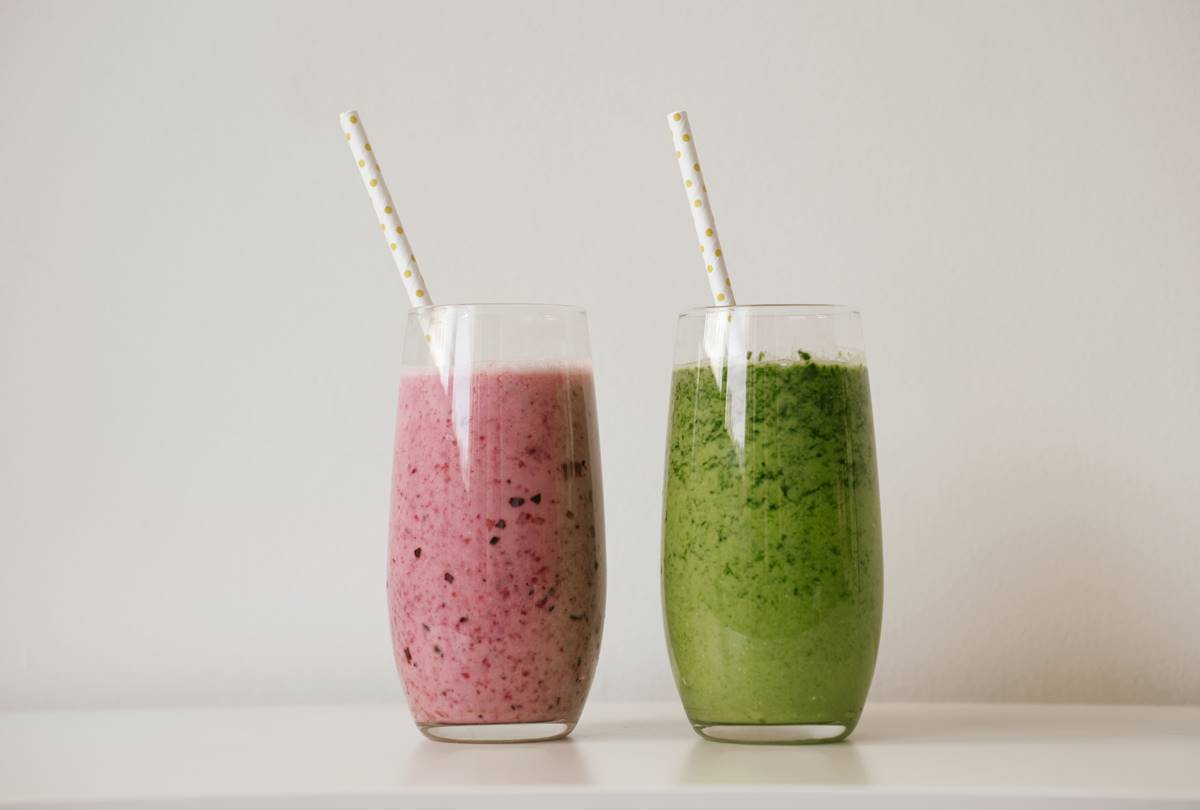 Foto colorida - Dois copos, um com uma bebida verde e outro com uma bebida rosa