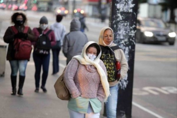 Mulher caminha em rua de São Paulo vestindo blusa, touca, máscara e cachecol. Ela tem as mãos no bolso - Metrópoles