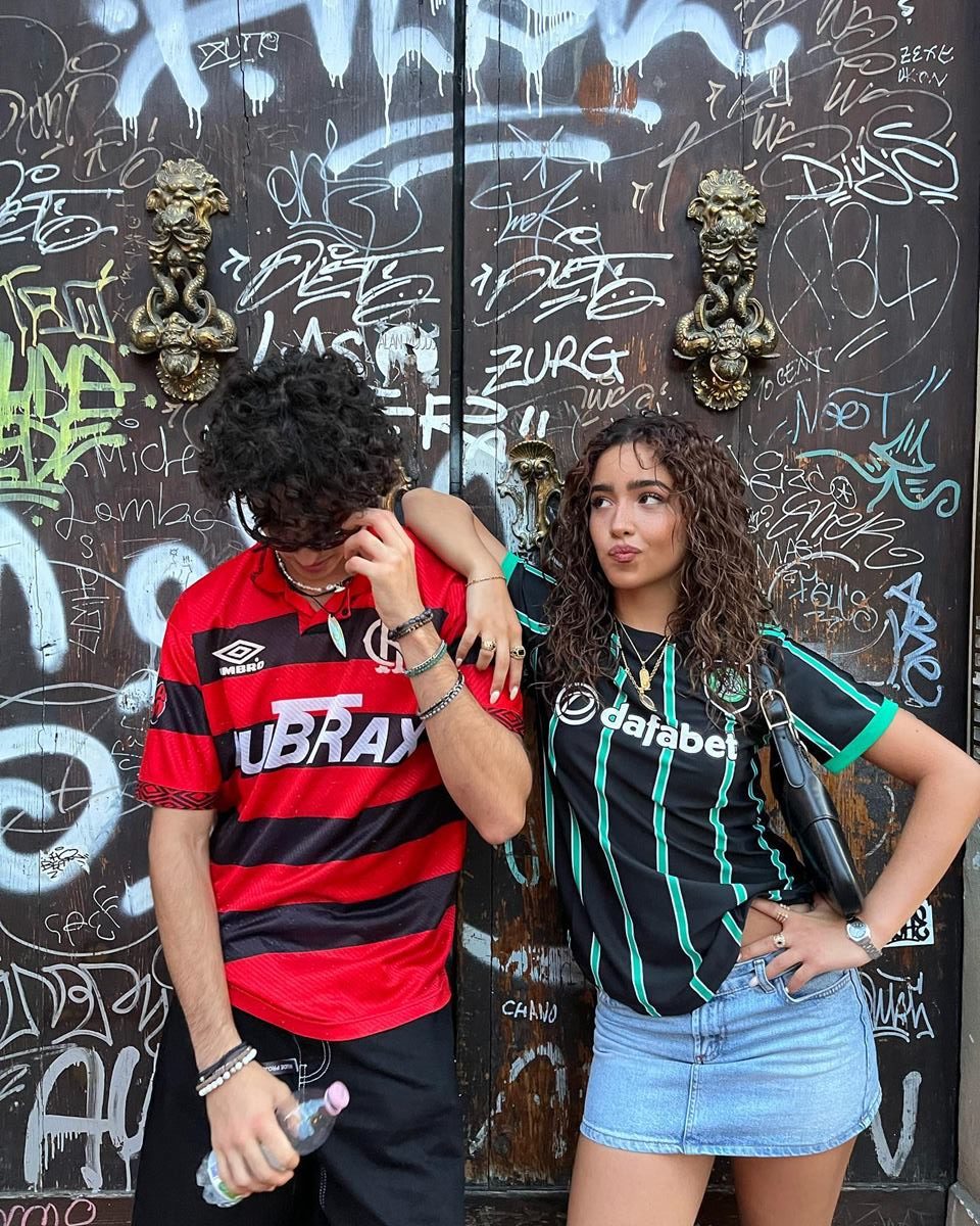 casal abraçado, a mulher usando uma camisa de time na moda tendência blokecore date encontro - metrópoles