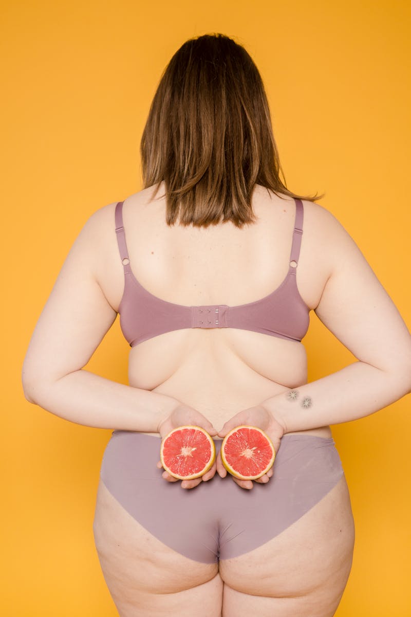 Mulher de costas para a foto usando roupas íntimas e segurando duas metades de laranja - Metrópoles