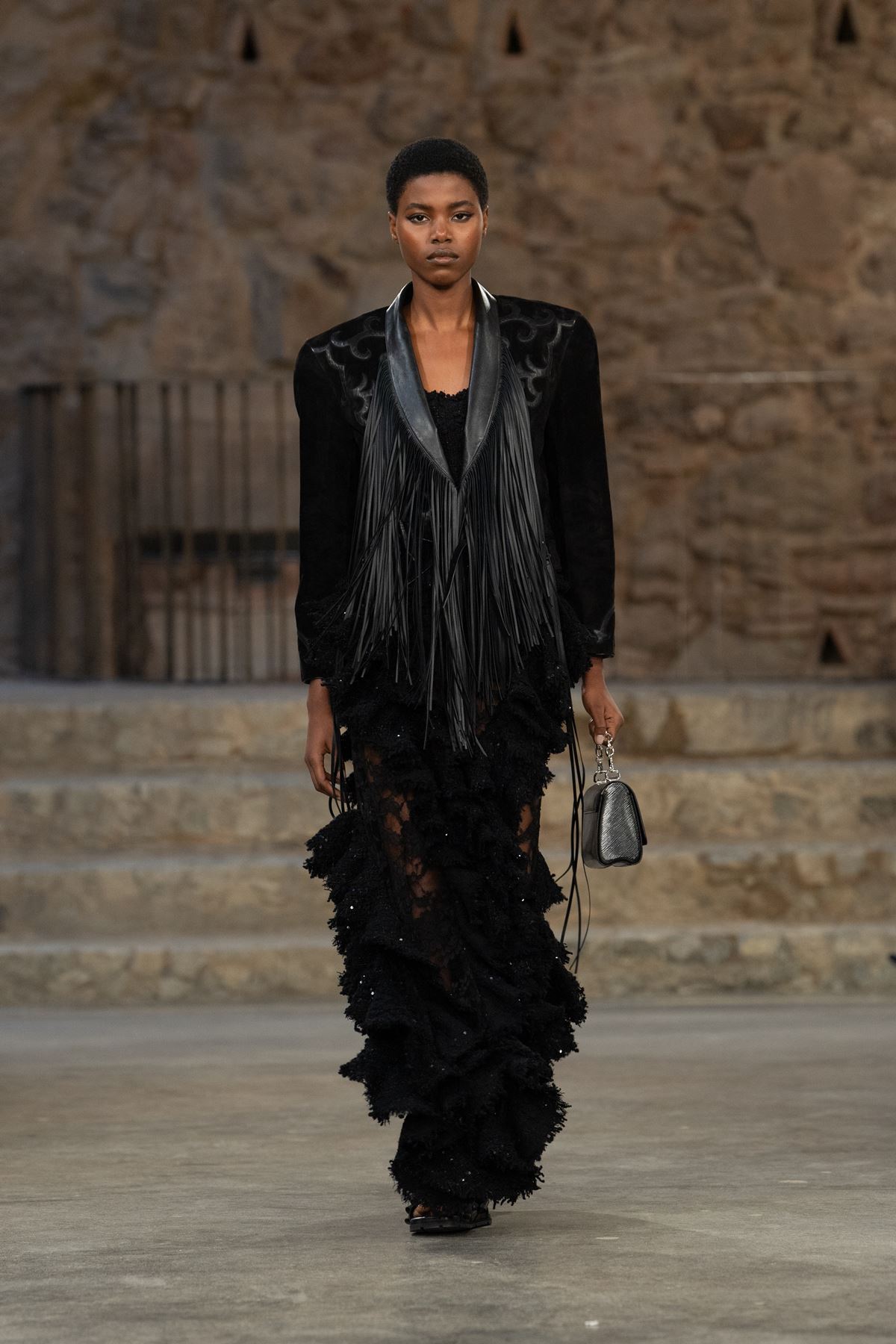Modelo na passarela da Louis Vuitton. Ela usa look preto com franjas e blazer - Metrópoles