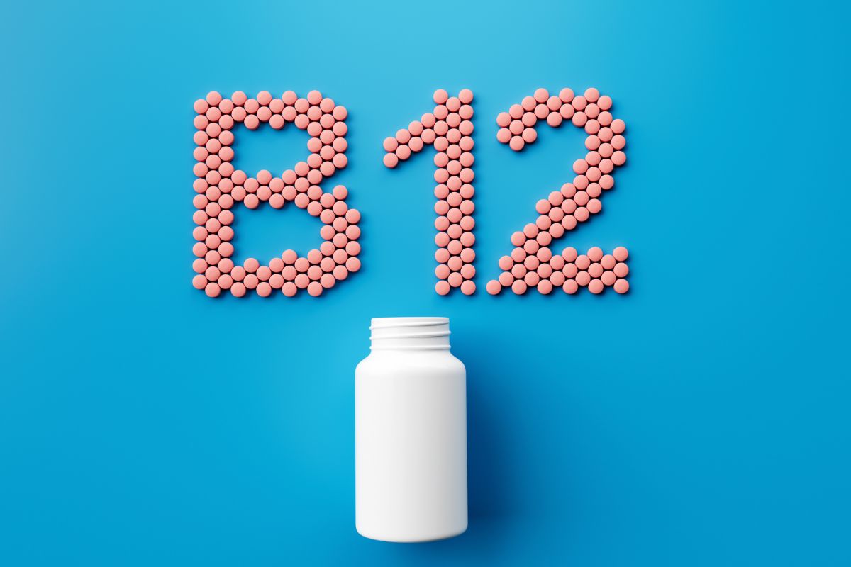 Foto colorida - Pote de remédio branco em um fundo azul, com comprimidos formando a palavra "B12"