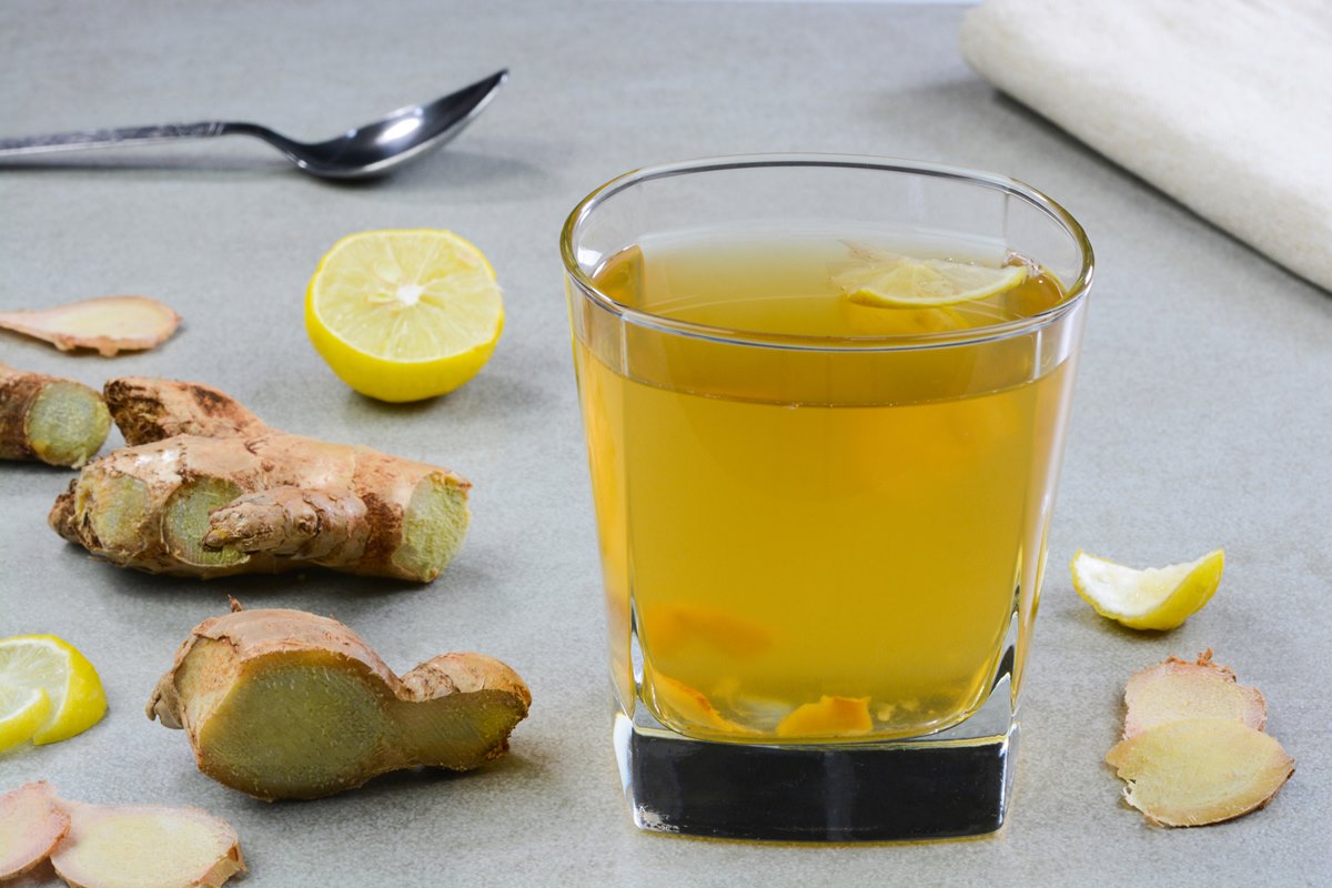 Foto colorida de copo com chá de gengibre e suco de limão. Ao redor, tem pedaços da raiz tuberosa e da fruta cítrica - Metrópoles