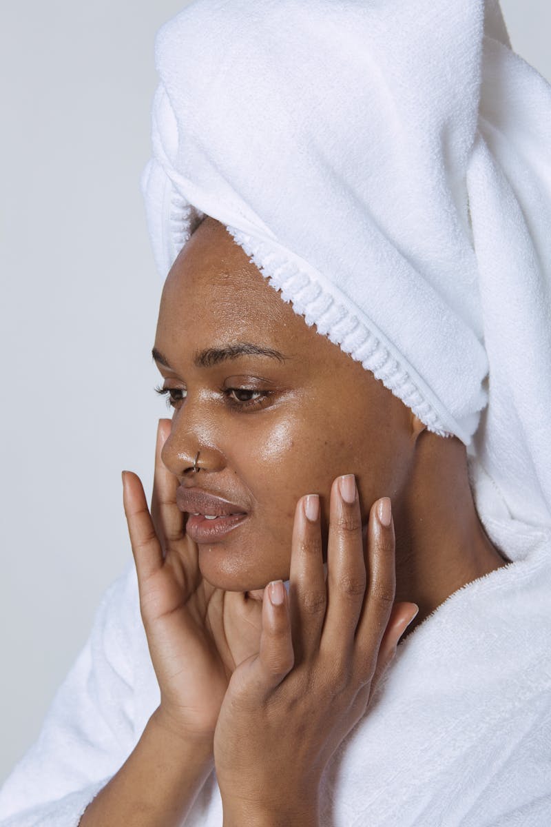 Jovem mulher negra com toalha no cabelo passando as mãos no rosto - Metrópoles