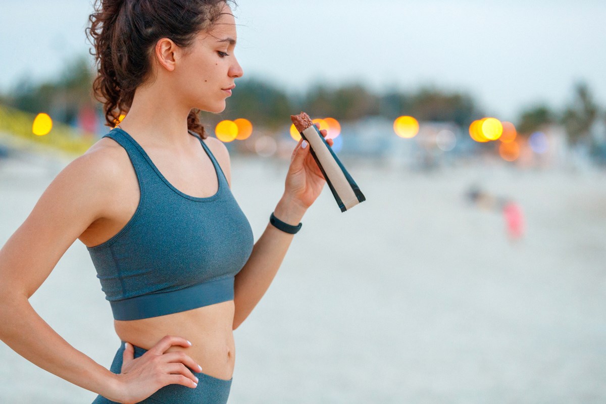 Foto de mulher com roupa de malhar e segurando uma barra de proteína - Metrópoles