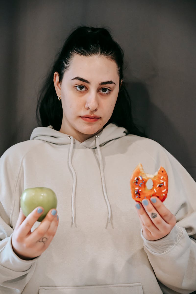 Jovem mulher segurando uma maçã e um doce nas mãos - Metrópoles
