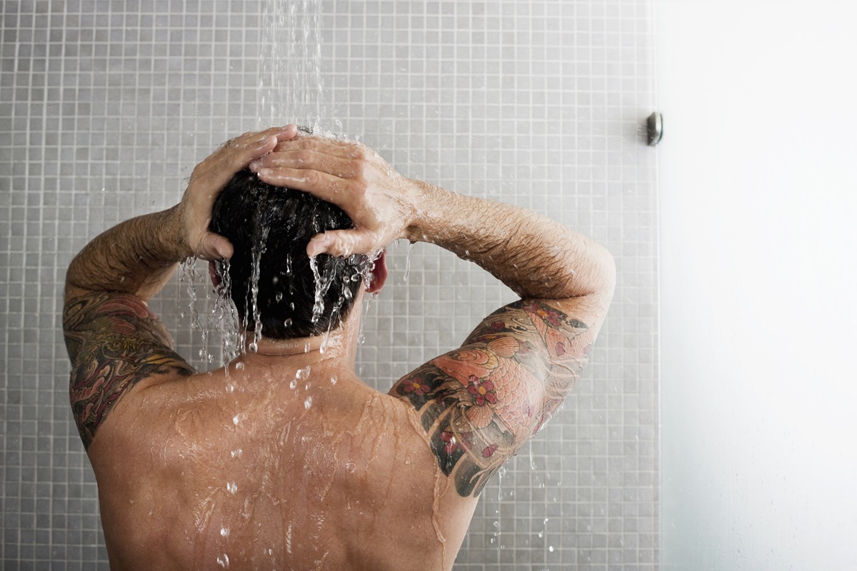 Foto mostra homem branco de costas enquanto toma banho e lava o cabelo