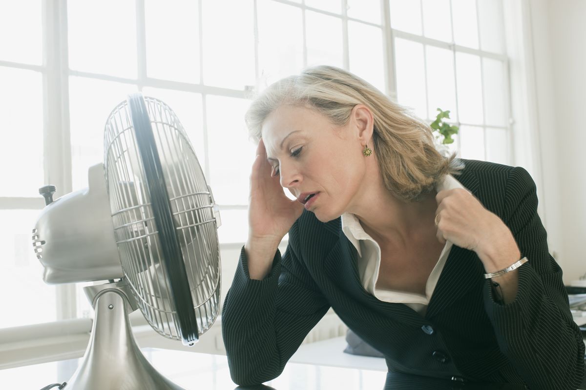 Foto colorida - Mulher branca e loira em frente a um ventilador sofrendo com a menopausa