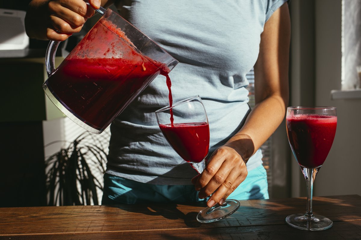 Foto colorida de mulher colocando suco de beterraba em uma taça. Outra taça já tem a bebida - Metrópoles