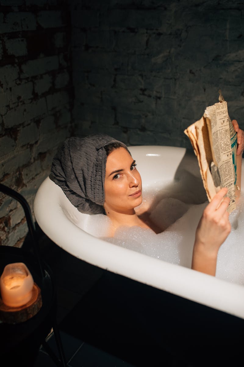 Jovem mulher deitada em banheira segurando revista antiga - Metrópoles