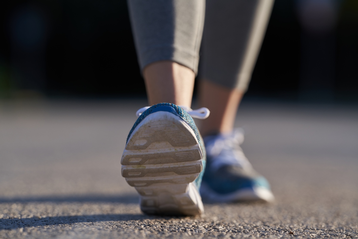 Foto em close-up mostra os tênis azuis de uma mulher durante caminhada