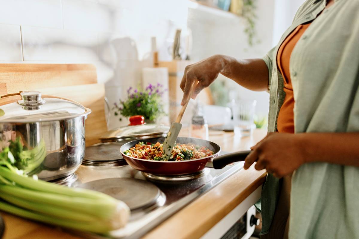 Foto colorida de uma mulher cozinhando - Metrópoles