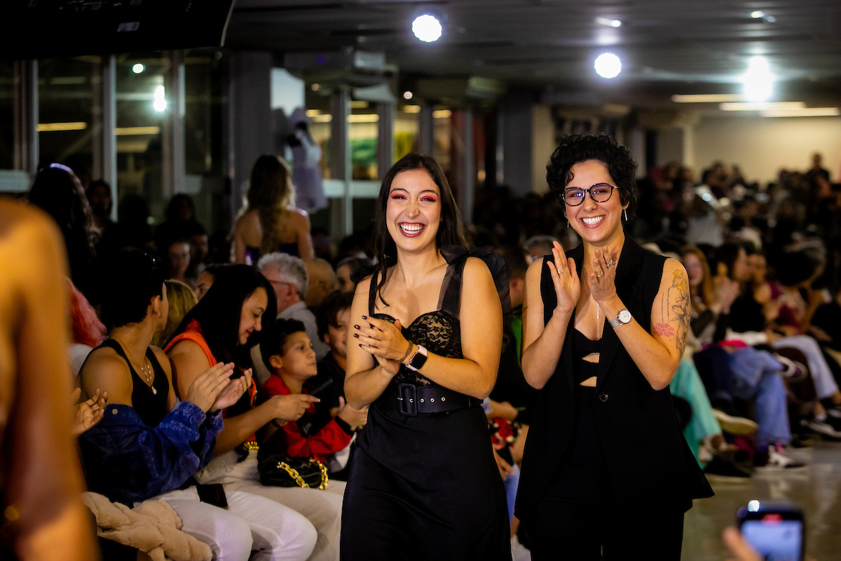 Dupla de alunas sorriem e caminha enquanto se aplaudem. Vestidas em preto, ambas andam lado a lado.