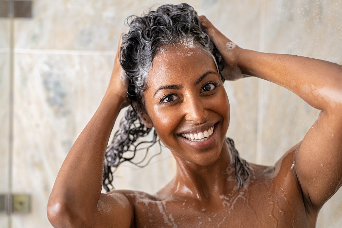 Foto colorida de mulher lavando o cabelo durante o banho - Metrópoles