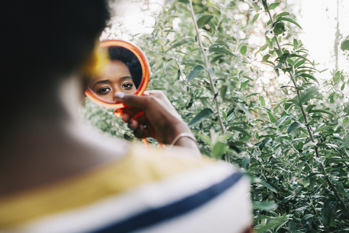 Jovem mulher negra segurando espelho pequeno - Metrópoles