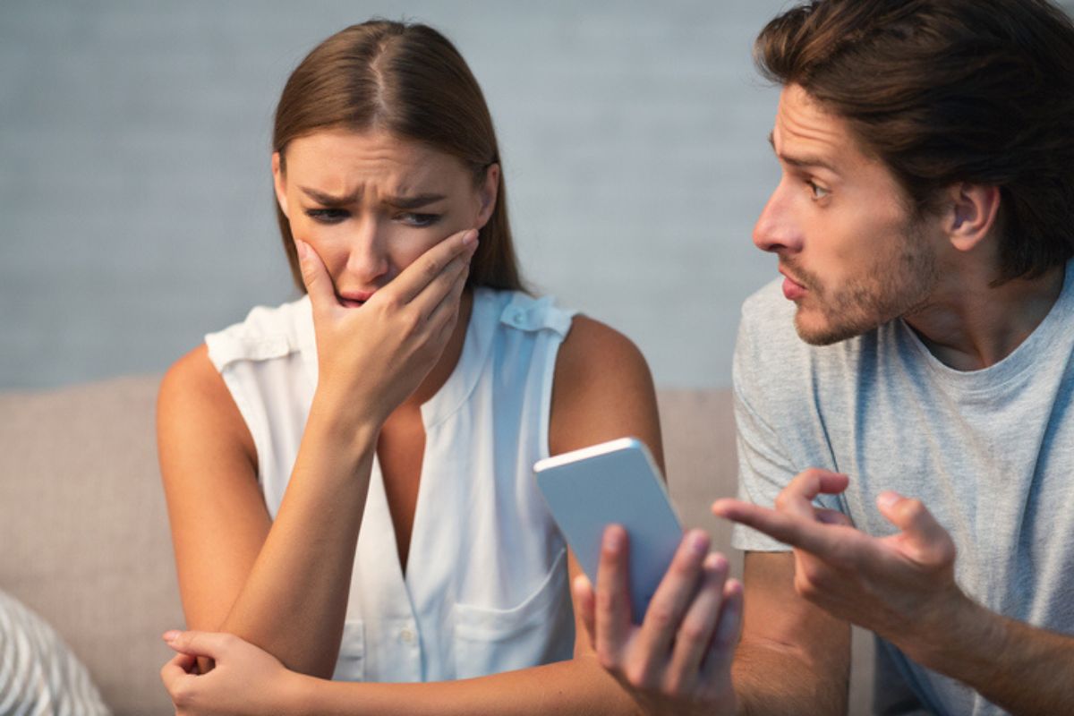 Imagem colorida de homem discutindo com parceira por algo no celular dela