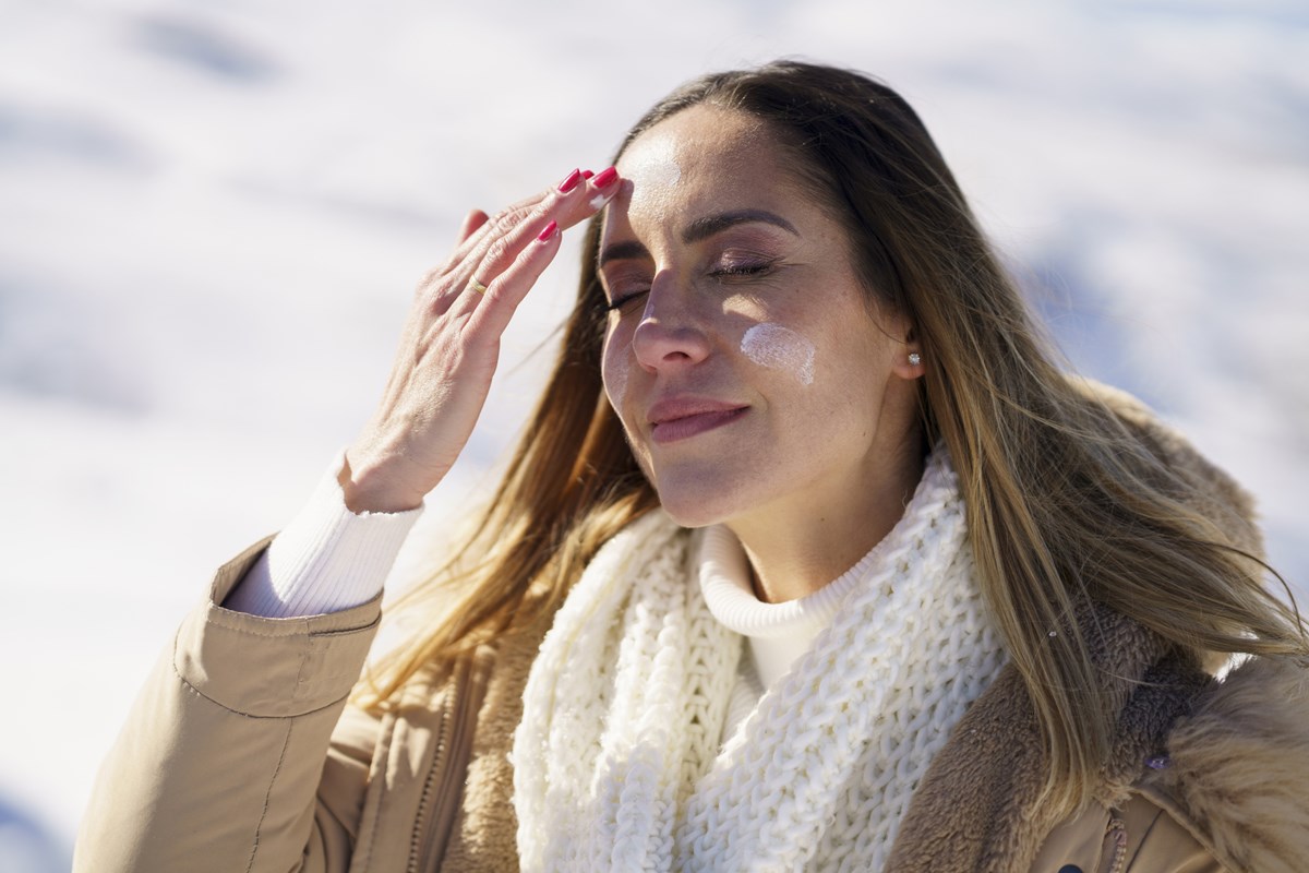 Foto colorida de mulher, com roupas de frio, passando protetor solar - Metrópoles