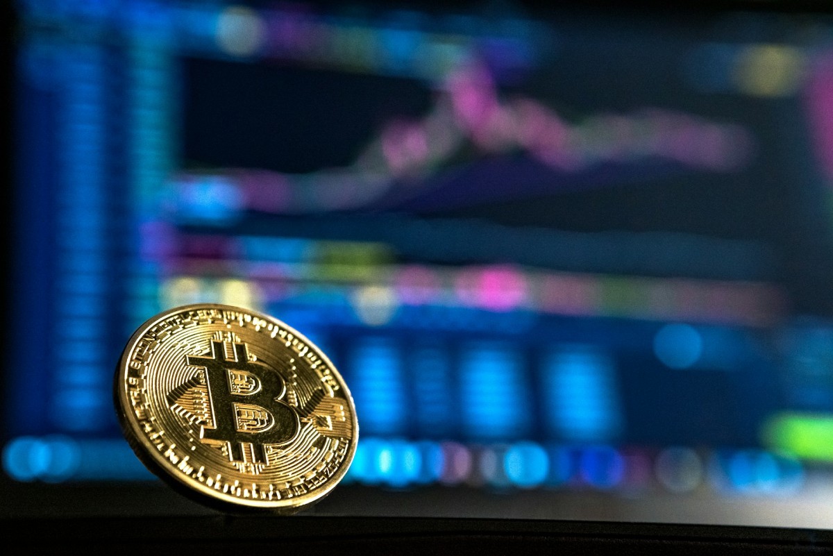 Fotografia colorida mostrando moeda de bitcoin em frente a computador-Metrópoles