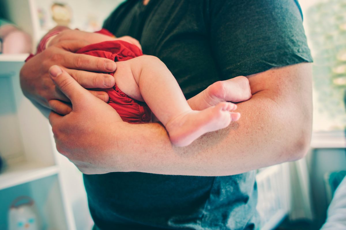 Foto colorida de um homem segurando um bebê - Metrópoles