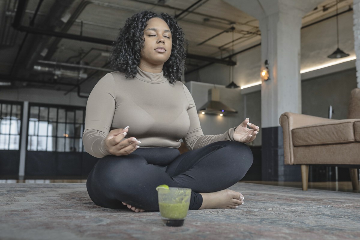 Foto colorida de mulher meditando e perto de um copo - Metrópoles