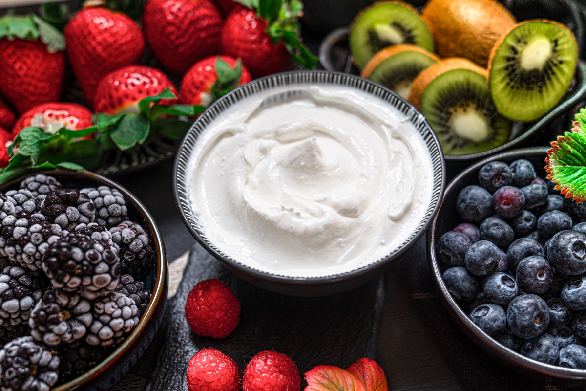 Foto de iogurte grego em potes de vidro com colheres, café da manhã saudável com iogurte grego fresco, muesli e frutas vermelhas no fundo