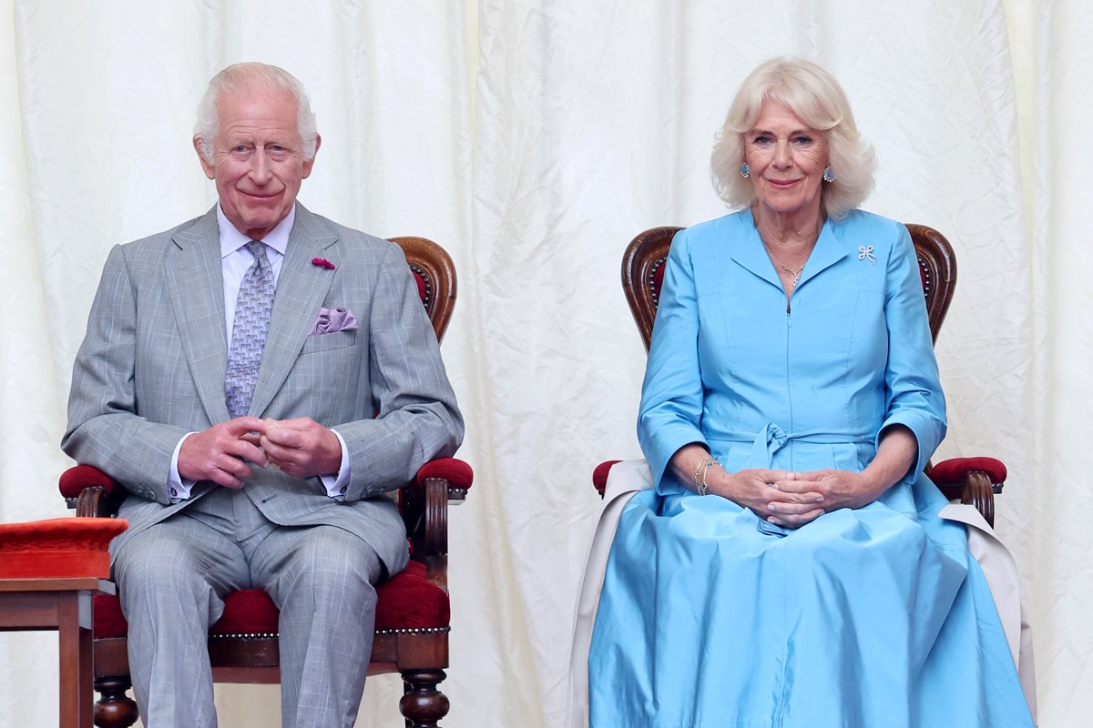 Foto colorida de homem de terno cinza e mulher de vestido azul-claro. Eles estão sentados - Metrópoles