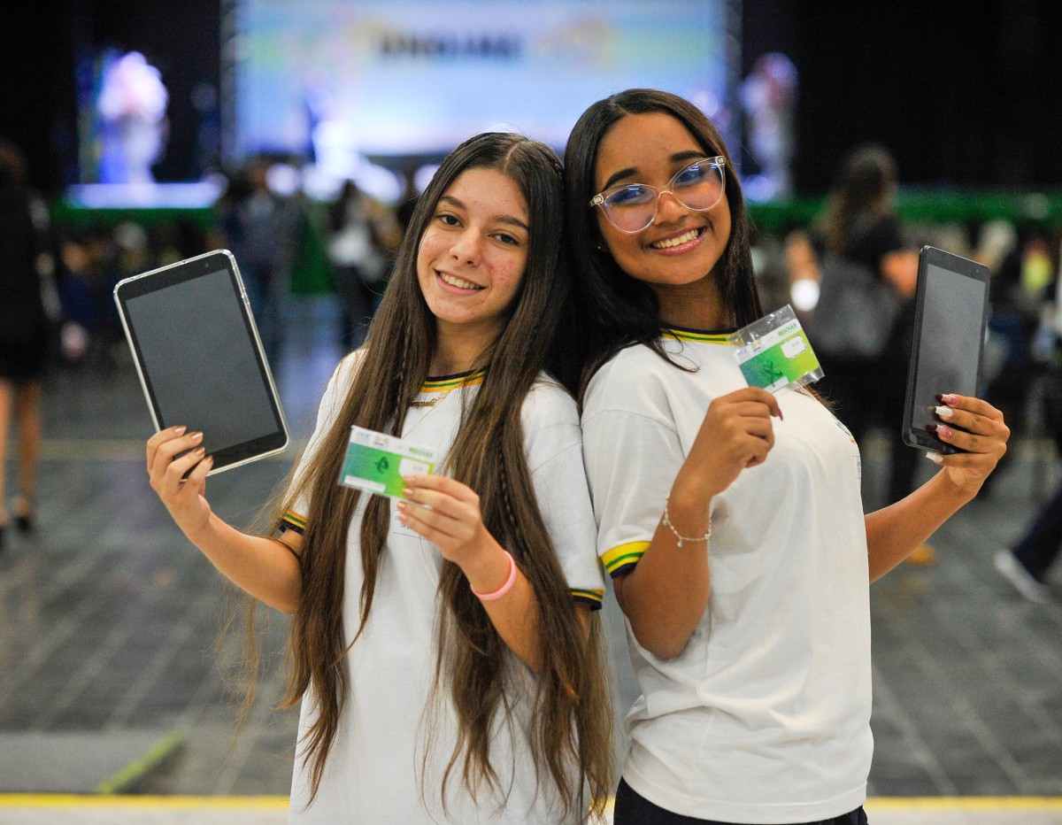 Fotografia colorida mostrando duas estudantes de costas uma para outra segurando carteira de estudante e material escolar-Metrópoles