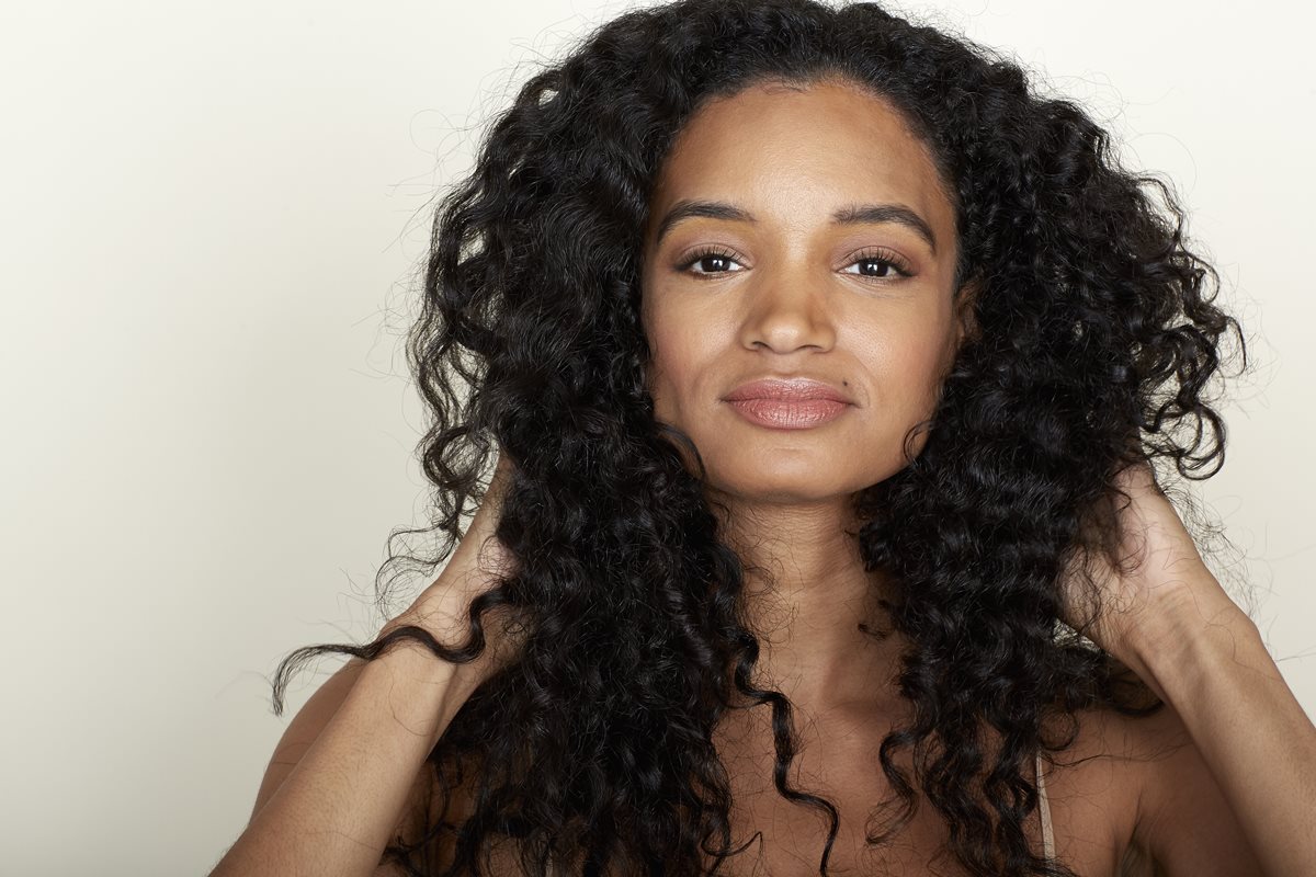 Foto colorida de mulher pegando no cabelo cacheado - Metrópoles