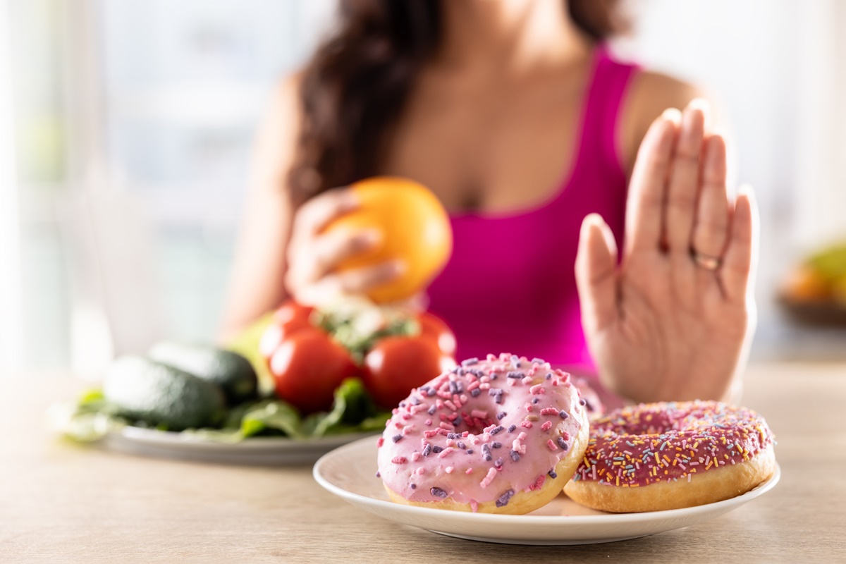 Uma mulher está determinada a perder peso recusando lanches doces e ricos em amido. A jovem recusa donuts doces e prefere vegetais frescos e saudáveis.